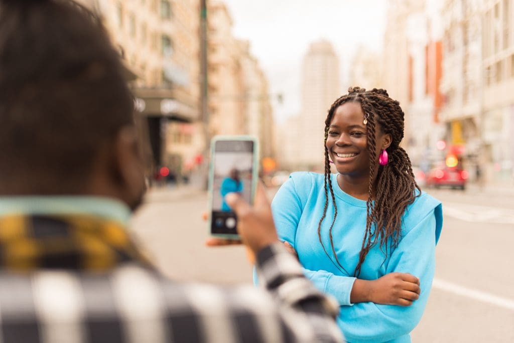tomando fotografía con celular a mujer en modo retrato con ciudad de fondo